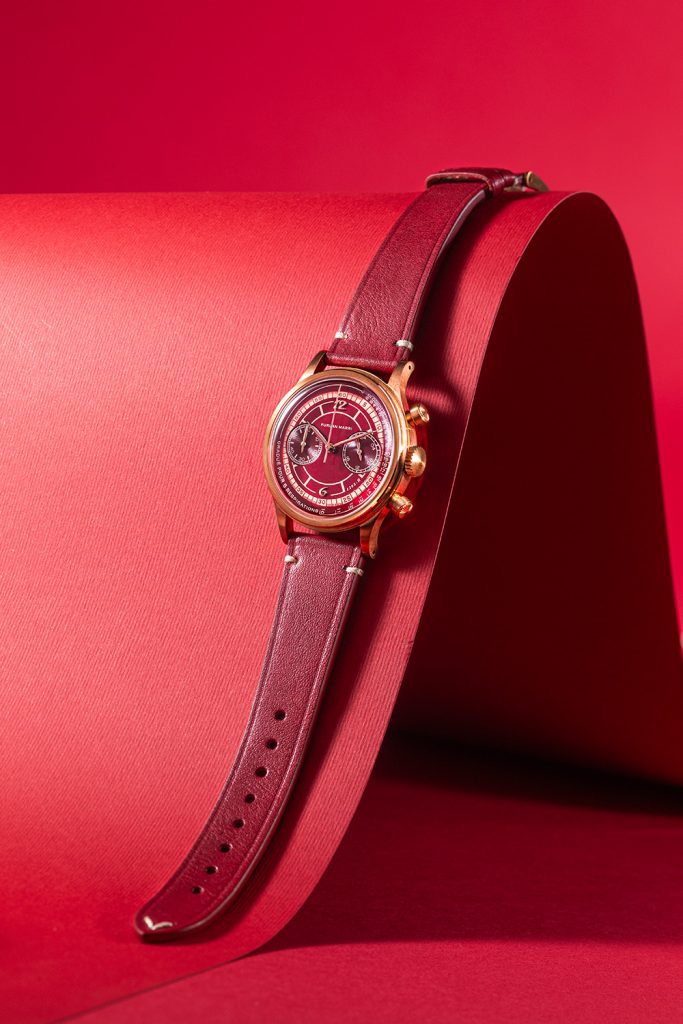 Bronze cased watch with burgundy dial and matching red leather strap against red background