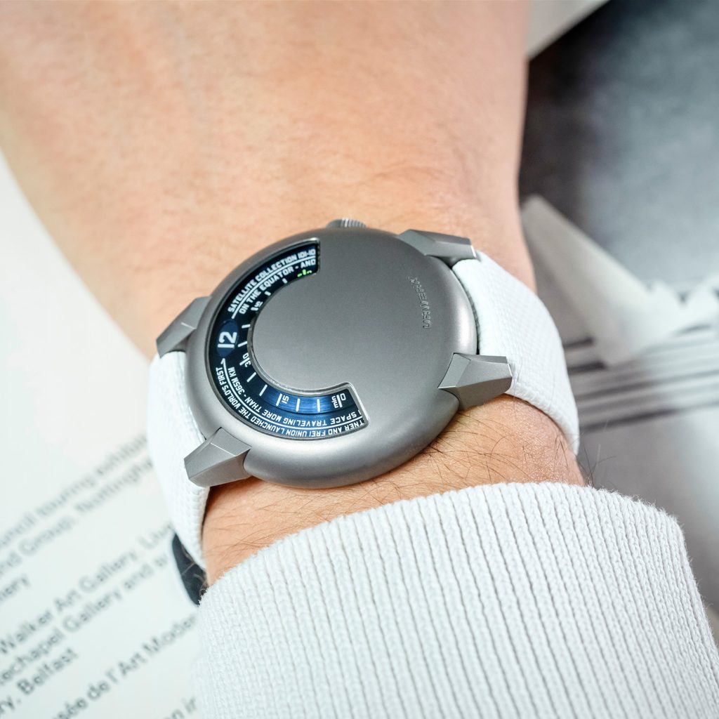 Titanium round shaped watch with blue semi-circular hour and minute indication on a wrist