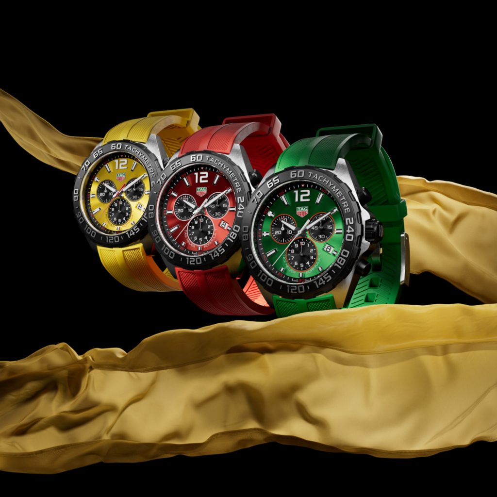 Three chronograph watches in yellow, red, green against black background with yellow silk fabric
