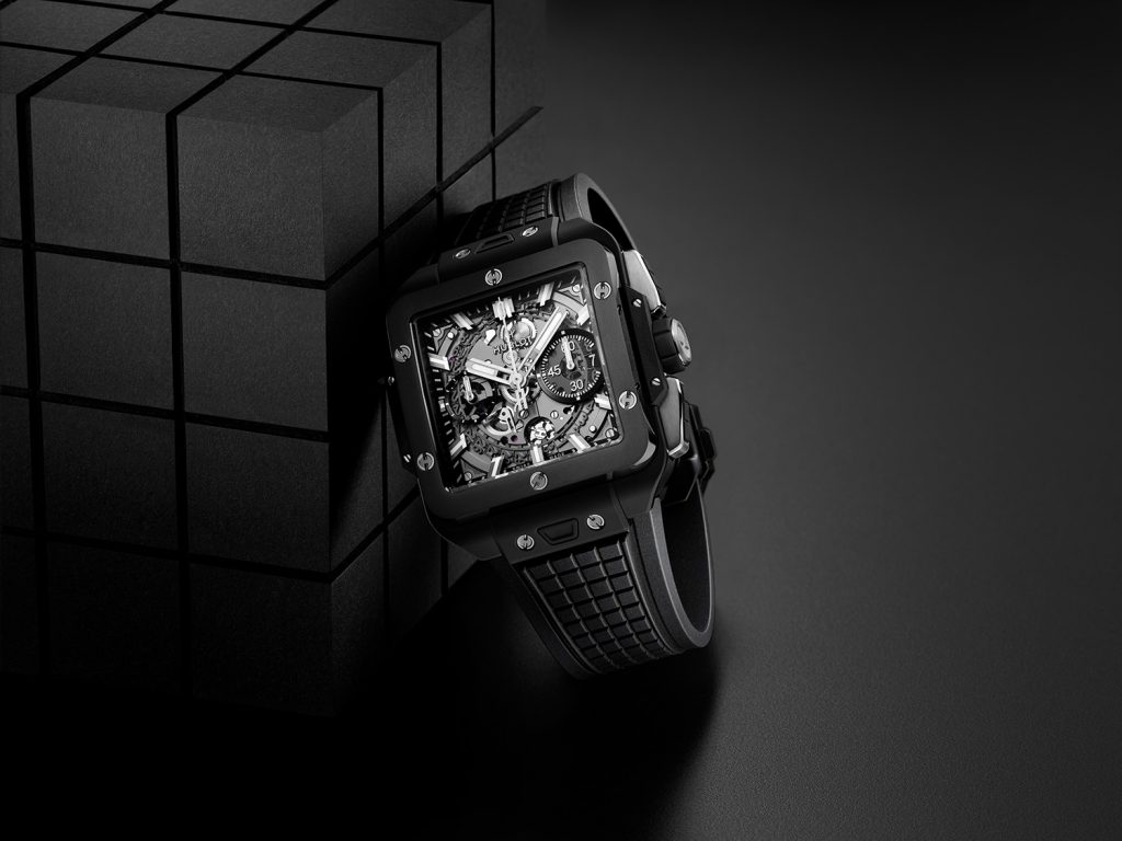 Square black ceramic watch with black strap against black backdrop